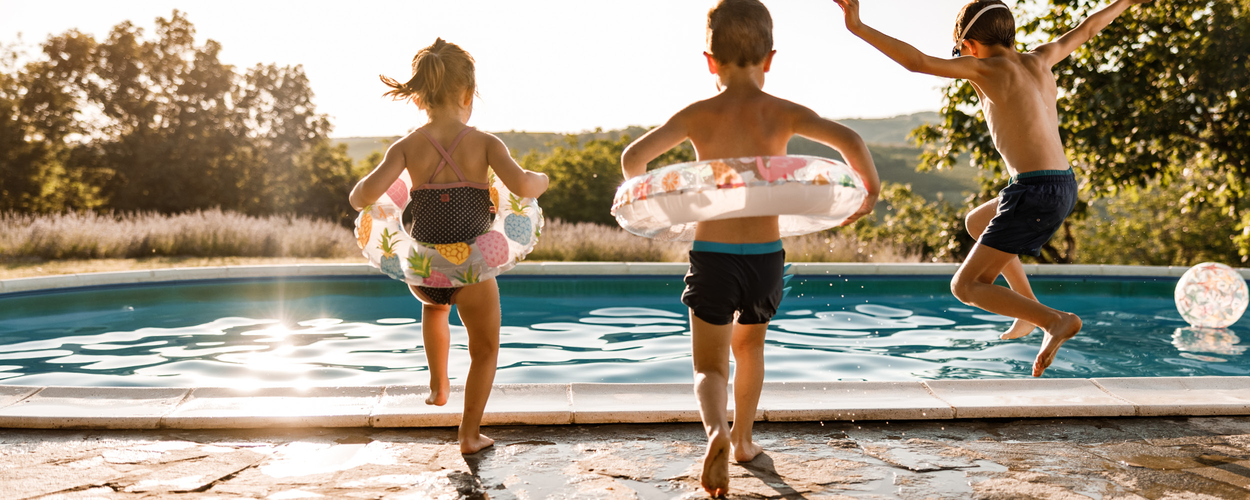 Enfants jouant près d'une piscine coque au soleil couchant, mettant en avant la sécurité avec des bouées et l'aménagement paysager, symbolisant ambiance estivale et détente familiale