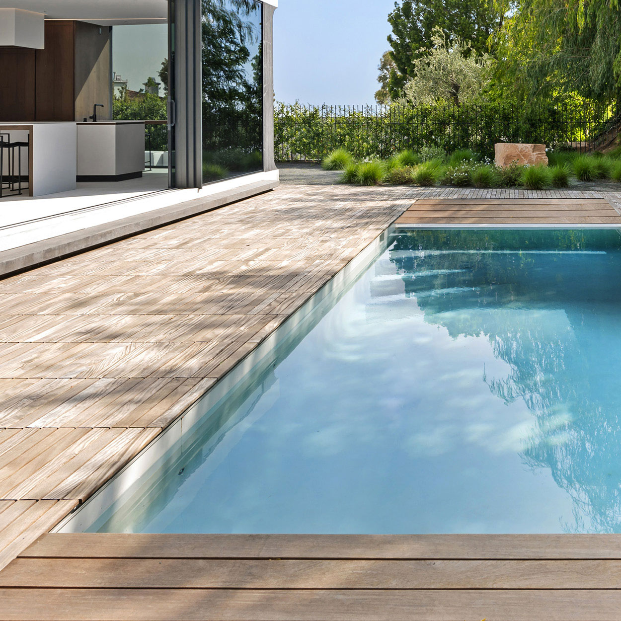 Piscine coque moderne avec revêtement en bois, intégrée harmonieusement dans un environnement élégant et verdoyant, ambiance luxueuse et apaisante